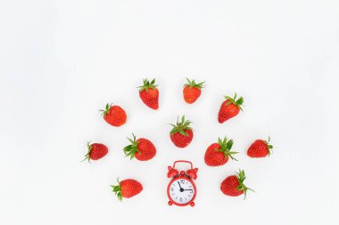 Kırmızı çalar saat ve beyaz arka plan üzerinde çilek berry saçılma uçan