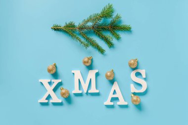 Metin Xmas beyaz harflerden, yeşil köknar dalı ve mavi arka plan üzerinde noel dekorasyon altın topları.