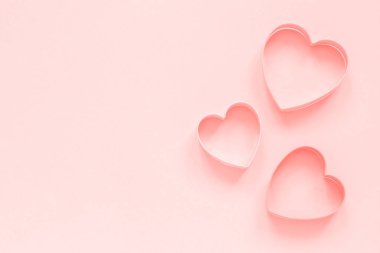 Pastel pembe arka plan üzerinde kalp şeklinde pembe kesiciler çerezleri