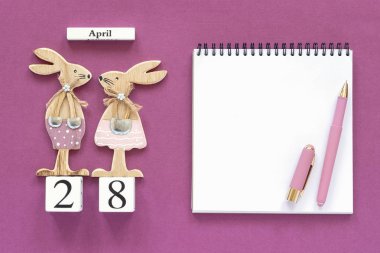 Takvim Nisan 28, çift ahşap paskalya tavşanları, mor kağıt arka plan üzerinde beyaz not defteri