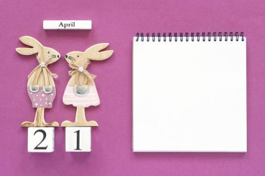 Takvim Nisan 21 ve ahşap paskalya tavşanları çifti, mor kağıt arka plan üzerinde beyaz not defteri