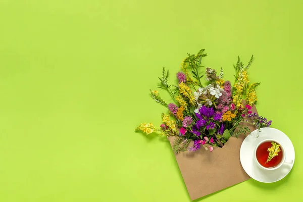 緑の背景にクラフトエンベロープとハーブティーのカップでフィールドカラフルな素朴なヴィンテージの花 — ストック写真