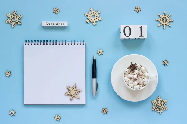 木製カレンダー 12月1日 マシュマロとスターアニスのココアカップ 青い背景にペンと雪片と空のオープンメモ帳 — ストック写真