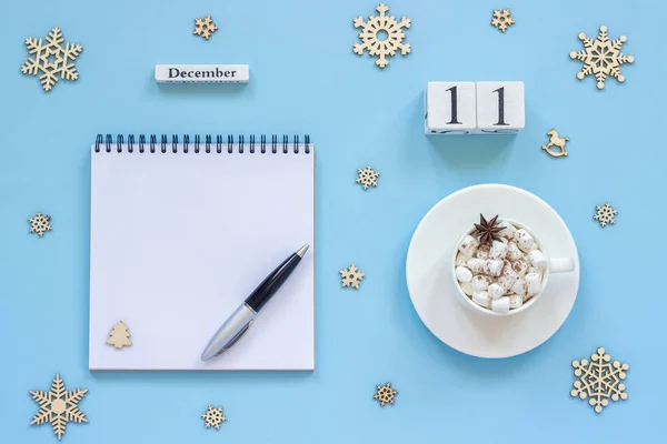 木製カレンダー 12月11日マシュマロとスターアニスのココアカップ 青い背景にペンと雪片と空のオープンメモ帳 — ストック写真