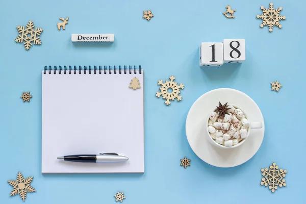 木製カレンダー 12月18日マシュマロとスターアニスのココアカップ 青い背景にペンと雪片と空のオープンメモ帳 — ストック写真