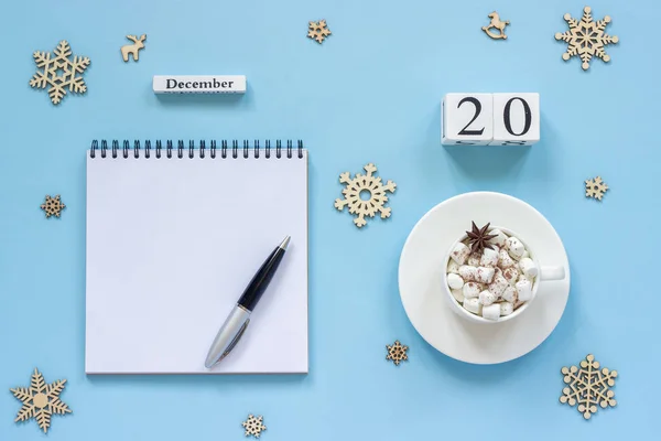木製カレンダー 12月20日 マシュマロとスターアニスのココアカップ 青い背景にペンと雪片と空のオープンメモ帳 — ストック写真