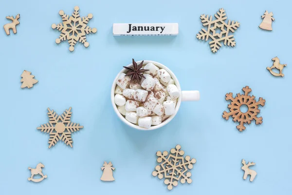 Wooden calendar winter month January, mug of cocoa with marshmallows and anise star surrounded by large wooden snowflakes on blue background.