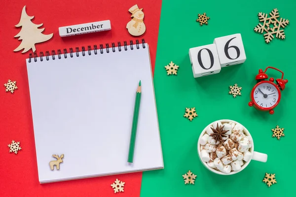 木製のカレンダー12月6日 マシュマロとココアのカップ 赤と緑の背景に目覚まし時計と空のオープンメモ帳 — ストック写真