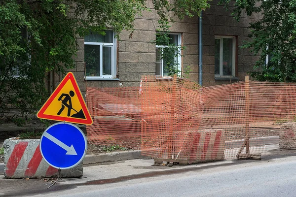 City street construction site with barricades, safety fence net, road work and detour signs.
