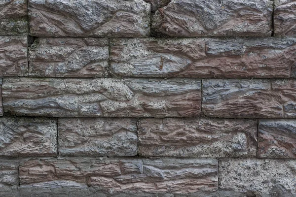 Imitation of brickwork from artificial stone in gray and brown shades with cracks and chips