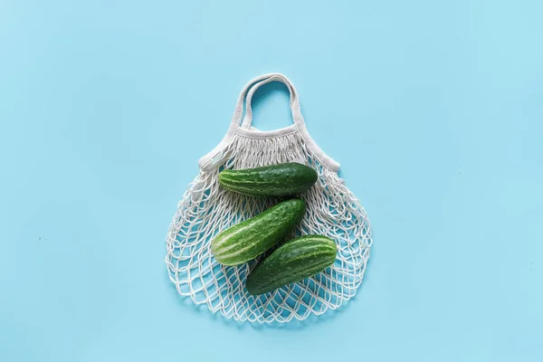 青い背景に再利用可能なショッピングエコフレンドルメッシュバッグに新鮮な緑キュウリ野菜。プラスチックや廃棄物ゼロをコンセプトにしています。コピースペース トップビュー フラットレイ — ストック写真