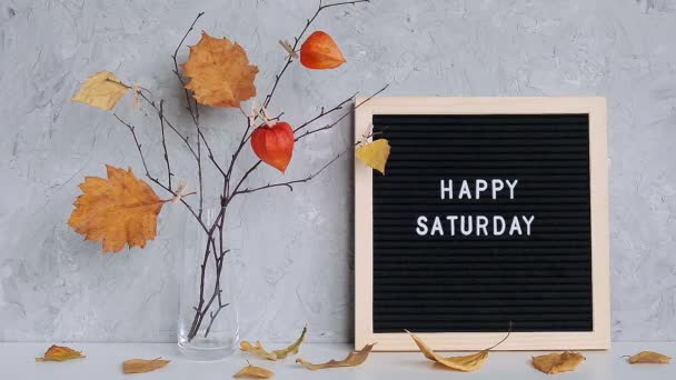 Happy Saturday text on black letter board and bouquet of branches with yellow leaves on clothespins in vase on table Template for postcard, greeting card Conceito Olá outono Sábado — Vídeo de Stock