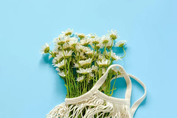 Bouquet of field daisies in reusable shopping eco mesh bag on blue background. Concept no plastic and zero waste. Copy space Top view — Stock Photo, Image