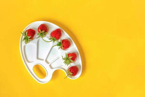 Fresas rojas maduras sobre una paleta artística sobre fondo amarillo con espacio para copiar. Concepto creativo pintura de colores de verano. Plantilla de laico plano para invitación de postales de diseño — Foto de Stock