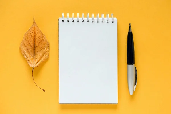 Sonbahar kompozisyonu. Beyaz boş not defteri, kurutulmuş turuncu yaprak ve kalem sarı arka plan üzerinde. Üst görünüm Düz lay Mockup Şablon u tasarımınız için — Stok fotoğraf