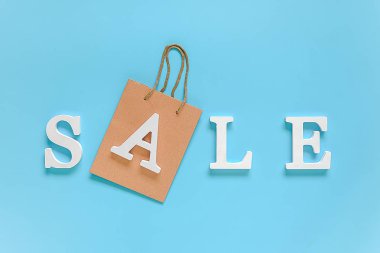 Metin Satış beyaz hacimli harfler ve mavi arka plan üzerinde kağıt alışveriş çantası. Üstten düz yatıyordu Copy space Concept indirimi. Metniniz, tasarımınız, reklamınız veya reklamınız için yaratıcı şablon