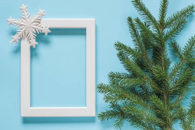 Mavi arka plan üzerinde dekorasyon kar tanesi ve yeşil ladin dalı ile beyaz çerçeve. Konsept Mutlu noel ler veya mutlu yıllar. Üst görünüm Düz lay Mockup Şablon tasarım, kart, davetiye için.