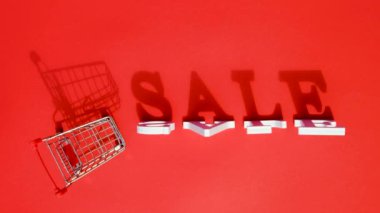 Küçük boş alışveriş arabası arabası sepeti, kelime Satış ve düşen beyaz harfler kırmızı arka plan üzerinde, büyük bir gölge atar. Konsept kara cuma satışı. Metniniz, tasarımınız, reklamınız veya reklamınız için yaratıcı şablon