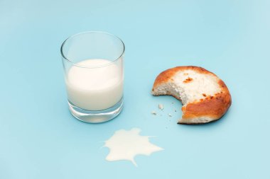 Yarım bardak süt, süzme peynir ile taze pişmiş çörek kapalı ısırılmış, mavi arka plan üzerinde süt ve kırıntıları dökülen. Konsept besleyici kahvaltı veya atıştırmalık