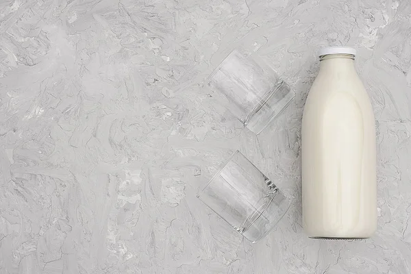 Milk in glass bottle and two empty glasses on gray background with copy space. Flat lay top view