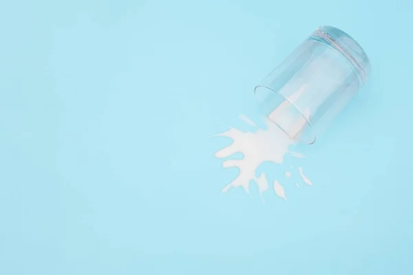 Spilled milk. Overturned glass with milk on blue background. Dairy abandonment concept Copy space Top view