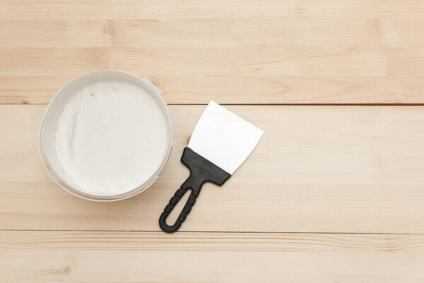 Spatula and a bucket of white putty on wooden boards. Top view Copy space