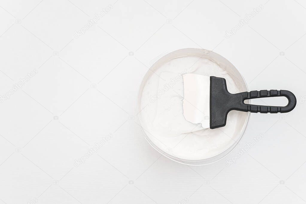 Spatula and a bucket of putty on white wooden boards. Top view Copy space
