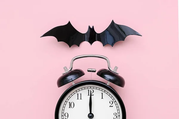 Halloween-Nacht-Konzept. schwarzer Wecker und fliegende Fledermaus auf rosa Hintergrund, Nahaufnahme. kreative flache Lage, Draufsicht, Vorlage für yuor Design, Grußkarte, Einladung — Stockfoto