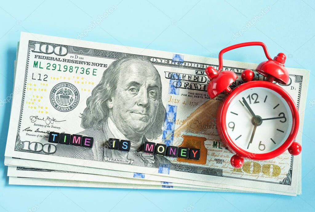 Time is money text and red alarm clock on background of American hundreds dollar bills, closeup. Creative concept quote of the day. Top view Flat lay Copy space