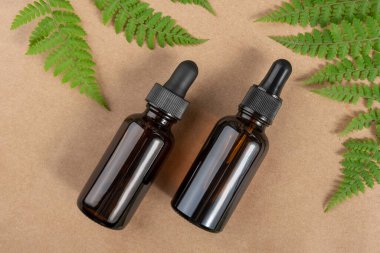 Serumlu iki kahverengi cam şişe, gerekli yağ ya da diğer kozmetik ürünler ve yeşil eğrelti otu yaprakları bej arka planda. Doğal Organik Spa Güzellik Konsepti Üst Görünüm Kopyalama Alanı.