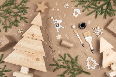 XMAS veya Yeni Yıl kompozisyonu. Tahta Noel ağaçları, boya, fırçalar ve bej arka planda köknar dalları. Kavram sıfır israfı, çevre dostu Mutlu Noeller. Üst Görünüm Düz.
