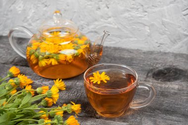 Bir fincan bitki çayı, şeffaf çaydanlık ve ahşap arka planda kadife çiçekleri. Calendula çayı sağlığınıza iyi gelir. Boşluğu kopyala.