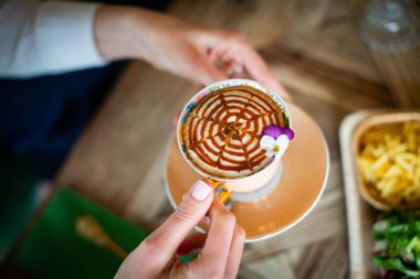 Ahşap masada kapuçino bardağı taşıyan kadın. 