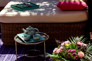 Küçük bir masaya mavi kil çayı ve açık terasta bir buket çiçek. 