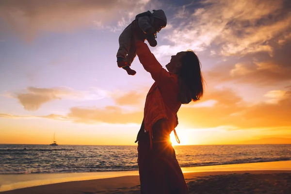 夏のビーチの海に日没で母と赤ちゃんのシルエット 女性と海のビーチで一緒に野外で遊ぶ子供 若い母親は 空に赤ちゃんをスローします 幸せな家族の背景 — ストック写真