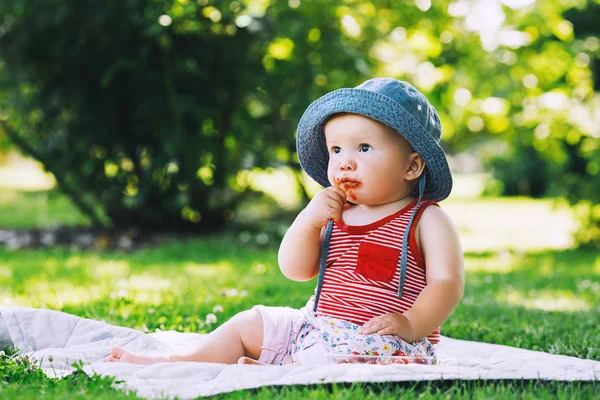 思いやりのある女の子が初めてで新鮮な赤いイチゴを食べるします 緑の自然の背景に夏の屋外での赤ちゃん 物思いにふける 困惑した子 子供の頃の画像です アレルギー製品のコンセプト — ストック写真