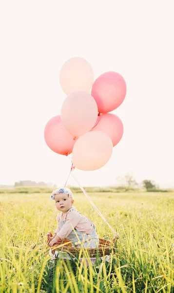 Baby girl in wicker basket with balloons on nature at summer — Stock Photo, Image