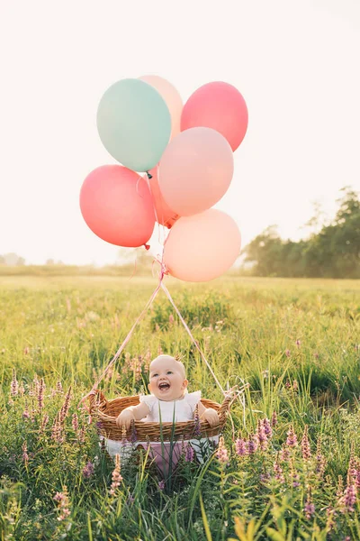 Девочка в плетеной корзине с воздушными шарами на природе летом — стоковое фото