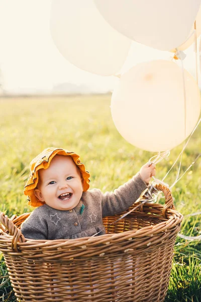 Bébé fille dans un panier en osier avec des ballons sur la nature en automne . — Photo