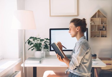 Kadın ev içi serbest ofis konsepti. Gözlüklü kız yeni bir projeyle çalışıyor. İş yerindeki bilgisayarlı minimalist tarzda planlayıcı veya günlükte kadın düşüncesi ve yazısı.