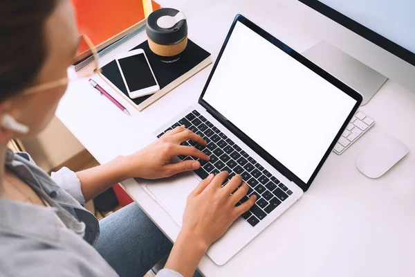 Woman using laptop with white blank screen, mockup. Female sitting at her working desk with laptop computer, cup of coffee, planner, smartphone. Distance education, online learning, studying concept.