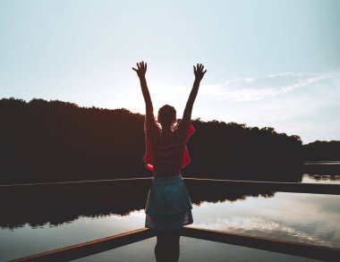 Genç bir kadın yeşil arka planda, gölün yanındaki tahta bir köprüde duruyor. Seyahat, özgürlük, yaşam tarzı konsepti. Dişi, açık havayı sever. Slovenya, Avrupa. Yurtiçi turizm