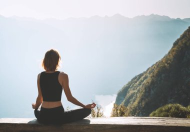 Doğada yoga yapan bir kadın. Genç kadın dağların arka planında meditasyon yapıyor. Sağlıklı yaşam tarzları, sakinlik, rahatlama, farkındalık, canlılık enerjisi..