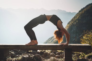 Doğada yoga yapan bir kadın. Dağlarda yoga yapan genç bir kadın. İnce, güçlü ve esnek vücutlu bir kız dışarıda spor yapıyor. Sağlıklı yaşam tarzları ve yaşam enerjisinin görüntüsü.