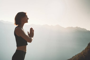 Doğada yoga yapan bir kadın. Genç kadın dağların arka planında meditasyon yapıyor. Sağlıklı yaşam tarzları, sakinlik, rahatlama, farkındalık, canlılık enerjisi..