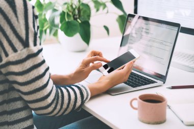 Çalışma masasında çalışan akıllı telefon ve dizüstü bilgisayarlı kadın ellerinin yakın çekimi. Kadın girişimci küçük işletme müşterilerin e-postalarına ya da telefonlarına cevap veriyor. Modern yaratıcı iş yeri.