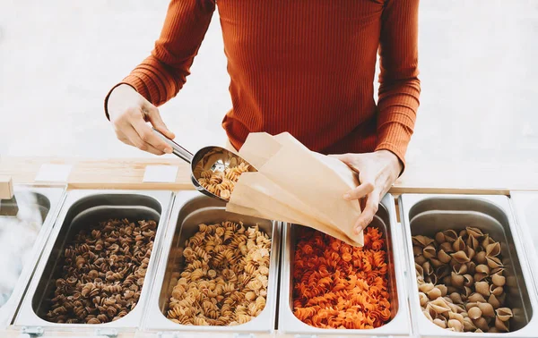 Woman is buying pasta in plastic free grocery store. Bulk foods in zero waste shop. Customer doing shopping without plastic packaging. Minimalist lifestyle. Sustainable small local businesses.