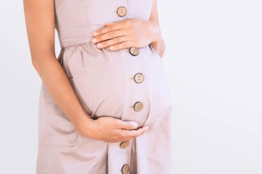 Elbiseli güzel hamile kadın beyaz arka planda el ele tutuşuyor. Anne doğumu bekliyor. Kadınlar hamileliğe hazırlanır. Hamilelik kavramı, doğum öncesi dönem, annelik sağlığı.