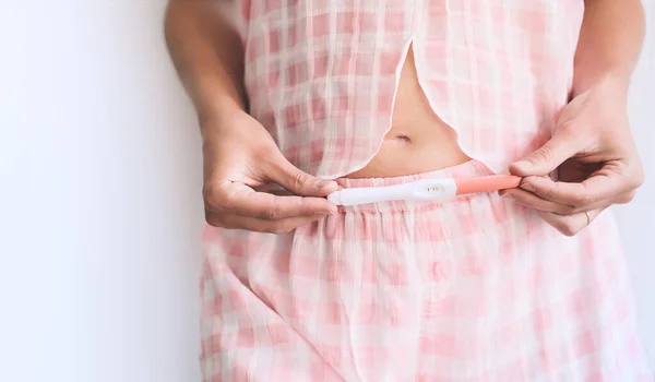 怀孕检测呈阳性的年轻女子双手紧握着腹部 怀孕准备和规划概念 — 图库照片