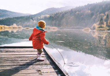 Çocuk sonbahar mevsiminde temiz ve soğuk havada dışarıda vakit geçirir. Küçük bir çocuk doğada balıkçılık yapıyor. Sağlıklı bir çocukluk. Aile hayatı. Dışarıda parkta su kenarında oynayan bir çocuk..
